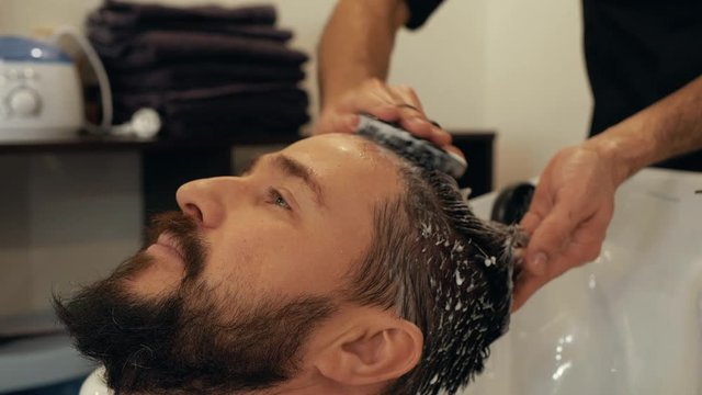 Male hairdresser massaging head to client special brash. Portrait bearded man washing head with shampoo in barber shop. Male stylist washing hair in barber salon. Head massage