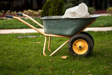 Naklejka premium A wheelbarrow with a sack for trash/ soil/ mulch/ compost/ fall leaves. Agricultural or landscaping works at backyard or park.