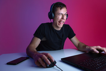 Gamer wearing headphones winking playing in a video game in a dark room lit with neon lights