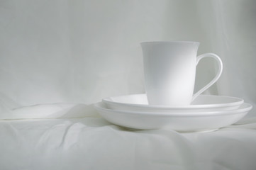 Fototapeta na wymiar white ceramic cup and plate on white fabric classic vintage still life background