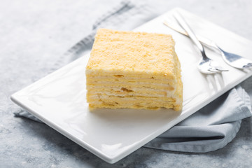 Piece of cake Napoleon on white plate on concrete              background, close up view. Traditional millefeuille dessert with puff pastry and custard, copy space.