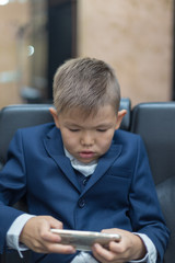 The boy uses the phone and plays games. Children are interested in online games and cartoons. A schoolboy in a school uniform and plays on a smartphone after school