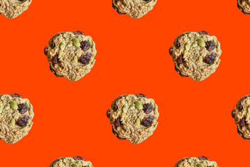 Seamless food pattern. Healthy oatmeal cookies with raisins, dried cranberries and pumpkin seeds. Gluten free snack for breakfast on trendy orange background