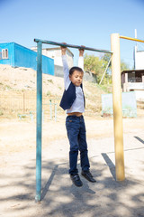 Portrait of a concentrated boy in school uniform, doing pull ups on horizontal bar outdoors. Healthy lifestyle concept