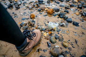 Selective focus of a lady wearing walking boots standing in a shallow rock pool on a sandy beach