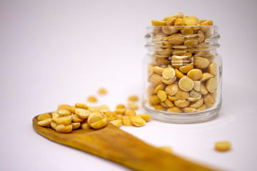 Dry peas are scattered from a jar on a wooden spoon on a white background. Close-up. Bio healthy and diet food. Selective focus.
