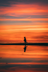 Little girl in a hat running on the sea shore in Baltics with a red and orange sky at the sunset