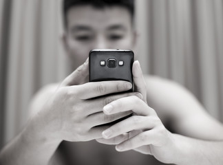 Handsome casual young man sitting at home, reading a sms on his mobile phone with a smile