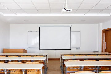 Classroom interior with projection screen, white board and wooden desks