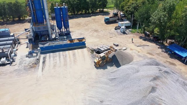 Asphalt plant from the top. Excavator pours out rubbles on the pile outdoors. Modern territory of asphalt factory surround by nature.