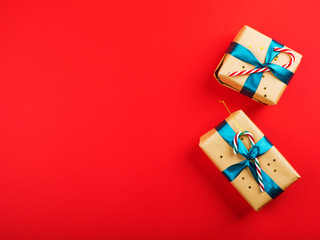 Christmas new year gift boxes wrapped in craft paper with green ribbon and candy canes on red bold color backdrop. Festive flat lay background with copy space. Design background