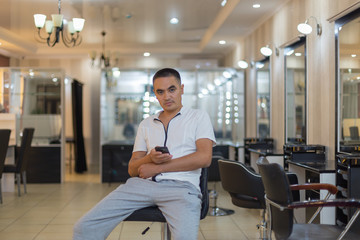 A man sits on a chair in the center of a beauty salon in the hands of a smartphone
