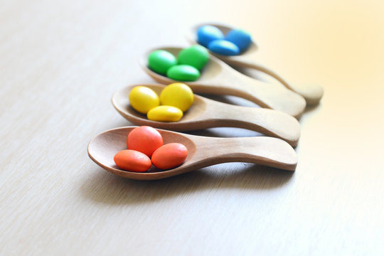 colorful button-shaped candies coated chocolate sweets in wooden spoon on wood table