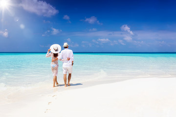 A hugging honeymoon couple walks down a tropical beach with turquoise sea and sunshine 