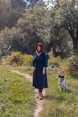 Naklejka na ściany i meble young woman with hat standing next to her dog in colorful forest 