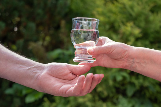 Hände reichen sich ein Wasserglas im Freien (Querformat)