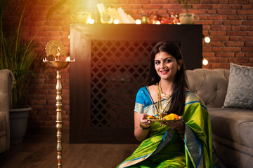 Indian Girl / women holding Pooja Thali while wearing green saree and sitting at home with flower...