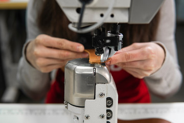 Sewing machine in a leather workshop in action with hands working on a leather details for shoes. Women's hands with sewing machine at shoes factory.