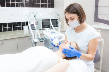 Beautician doctor doing rf-lifting procedure for flawless woman face laying in a beauty salon. Patient receiving electric facial massage. Skin rejuvenation and wrinkle smoothing.