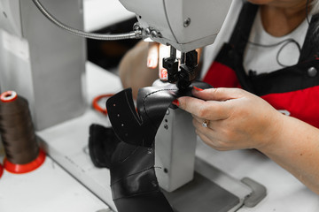 Sewing machine in a leather workshop in action with hands working on a leather details for shoes. Women's hands with sewing machine at shoes factory.
