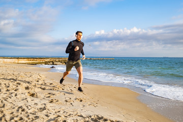 Fit male runner training on the summer beach and listen to music against beautidul sky and sea