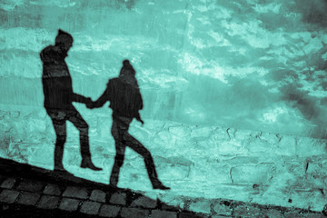 Funny or spooky shadow silhouette of love couple carefully walking down the hill or sneaking against grunge moon lit turquoise blue wall background - Happy Halloween card backdrop