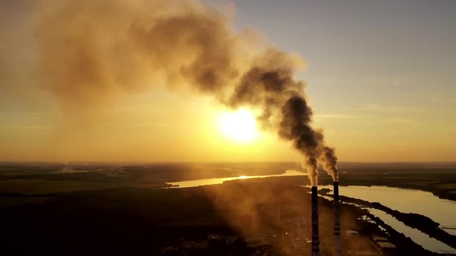 Industrial pipes with thick smoke at sunset. Two large pipes produce chemical smoke in the air on nature background. Environmental pollution.