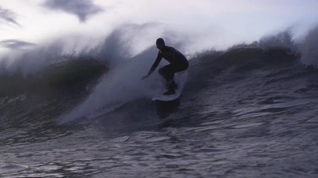 Slow motion footage of a surfer surfing past the camera in the evening light  in cold water