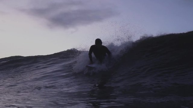 Surfer pops up and catches a wave in the dusk / twilight hours of the evening surfing a shortboard
