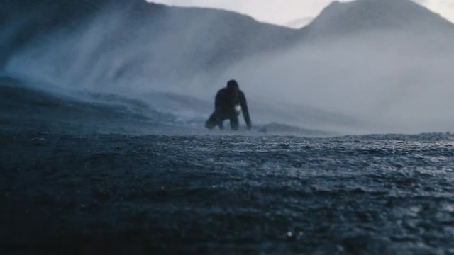 Surfer exits a wave and paddles back out to sea as a cloud of spray engulfs him in the evening light