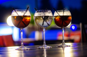 Beautiful row line of different colored alcohol cocktails on a party, martini, vodka,and others on decorated catering bouquet table on open air event, picture with beautiful bokeh