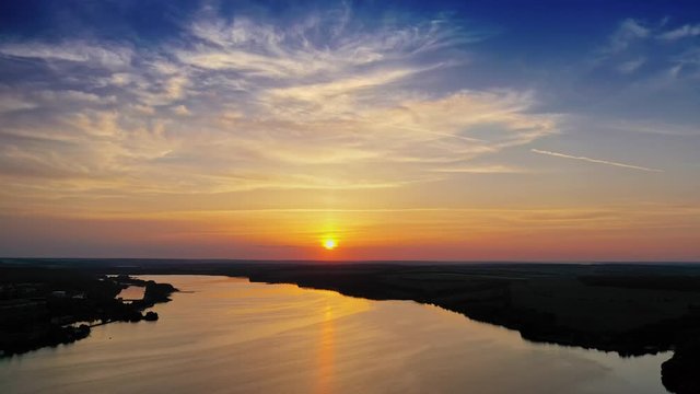 Amazing orange sunset over the river. Magic aerial view of evening sun among clouds. Golden path of setting sun on the calm river in nature. Slow motion camera.
