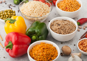 White bowl plates with boiled long grain basmati rice with vegetables and mushrooms on light table background with sticks and paprika pepper with corn,garlic and basil. Healthy vegan food.