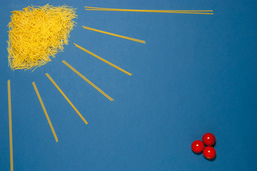 sun concept made of spaghetti and pasta, cherry tomatoes lie nearby