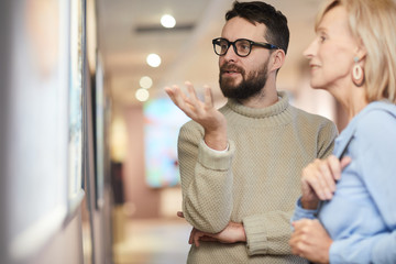 Waist up portrait of mature bearded man looking at paintings while enjoying exhibition in art...