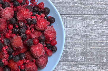 Plate with frozen berries mix and copy space area for captions and recipes. Natural fruit ingredient for cooking. Raw icy strawberry, red and black currant, chokeberry. Top view.