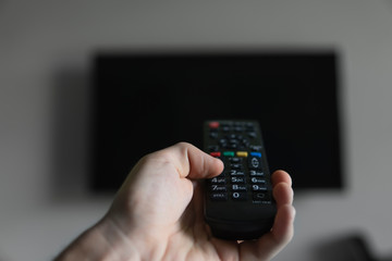 The man with the remote control in hand want switch on the TV and presses the button on the remote control. Remote control in hand closeup.