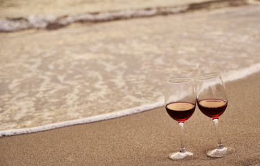Wine glasses with red wine on sand on the beach. Valentine's Day concept.