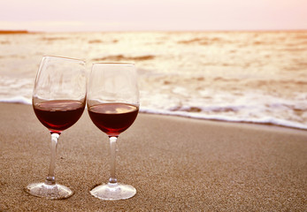 Wine glasses with red wine on sand on the beach. Valentine's Day concept.