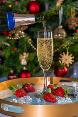 Champagne poured into glass with strawberries on festive background