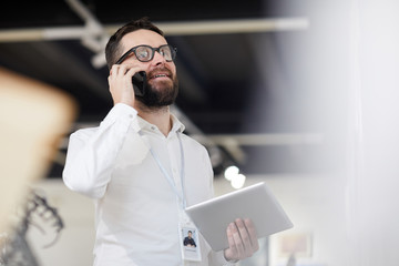 Low angle portrait of bearded art gallery manager speaking by phone while organizing exhibition in...