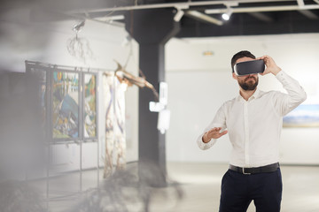 Portrait of modern bearded man wearing VR gear while enjoying immersive experience during...