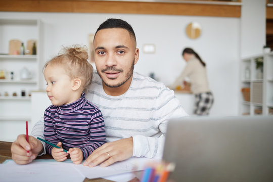 Portrait of loving mixed-race father looking at camera while drawing pictures with cute little girl at home, copy space
