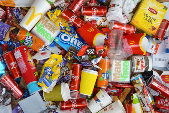 Big pile of many disposable colored trash from edible products of famous food and beverage manufacturers. Soda cans and chocolate bar wrappings in stack