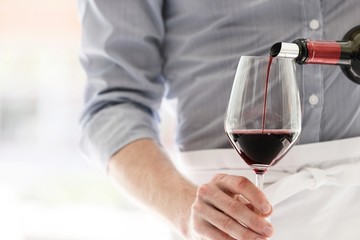 Midsection of waiter pouring red wine in wineglass at restaurant