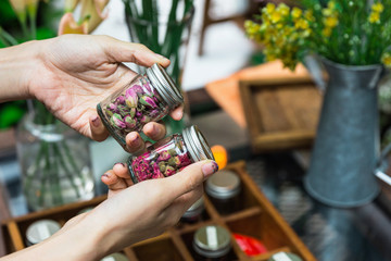 A woman choosing dry flowers for making flowering tea in glass bottles with aluminium lid on her hands.