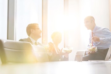 Smiling business colleagues eating lunch while sitting in boardroom during meeting at office