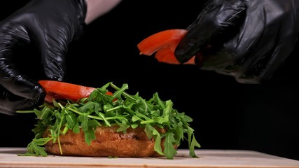 Craft burger is cooking on black background. Consist: sauce, arugula, tomato, red onion, bacon, red...