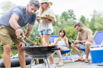 Man preparing food in barbecue grill with friends on pier