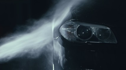 Car headlight wash. Washing modern vehicle body by high pressure jet wash hose water. Auto glass...